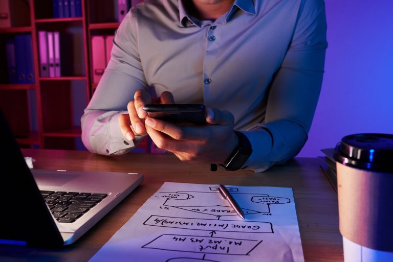 Mid-section of a man using a smartphone to take a picture of a work plan on his desk.